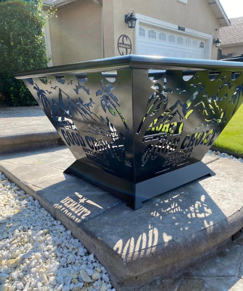 CNC Plasma Cuts - Black metal fire pit with a decorative cut-out design featuring palm trees and waves