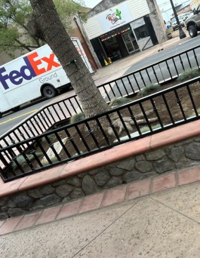 Black metal fence surrounding a tree on a city sidewalk, with a FedEx truck parked nearby
