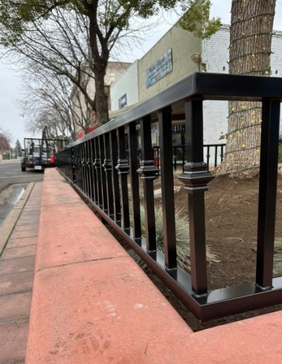View of a black metal fence encircling a tree, with a FedEx truck and a restaurant in the background