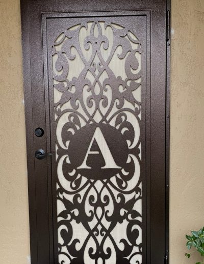 Ornate metal security door with a decorative cut-out pattern and a monogram