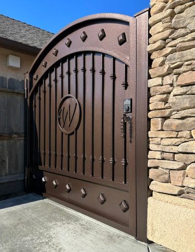 A decorative metal gate with an arched top and a wood-like finish, next to a wooden fence