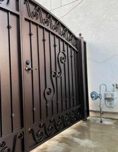 A metal gate with ornate details and a wooden panel, leading to a residential property