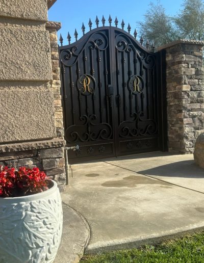 A view of a metal gate with a wood-like finish, next to a wooden fence and a satellite dish