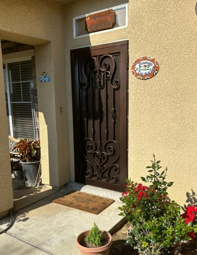 Metal security door with an intricate design and a monogram, enhancing home security and aesthetics