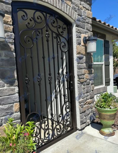 Ornate wrought iron gate with an arched top and decorative scrolls, leading to a home with stone accents
