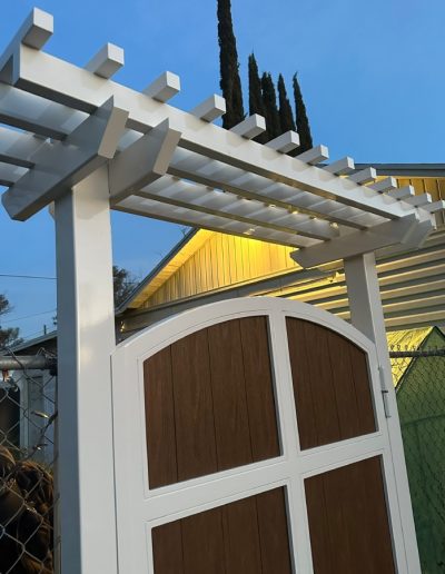 White vinyl pergola with a lattice roof over a wooden gate, adding a charming entrance to a backyard