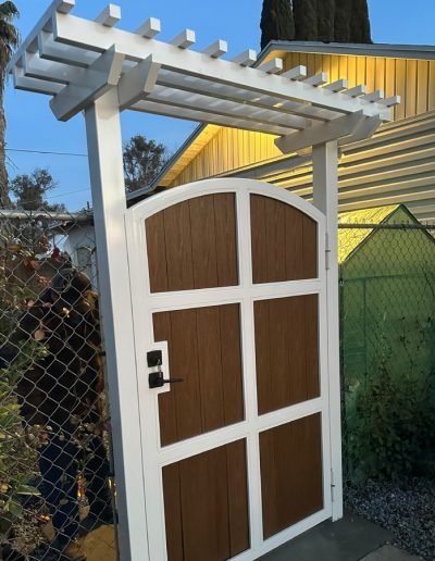 Pergola with a white vinyl frame and lattice roof, creating a shaded entryway with a wooden gate