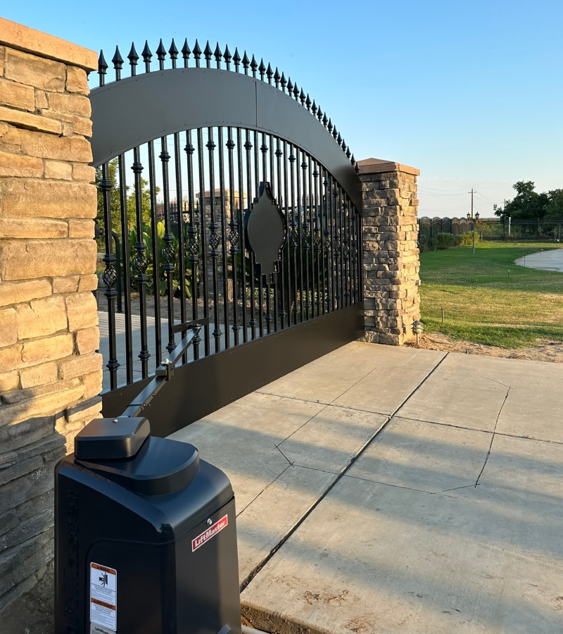 Black metal double driveway gate with an arched top, opening with an automatic gate opener