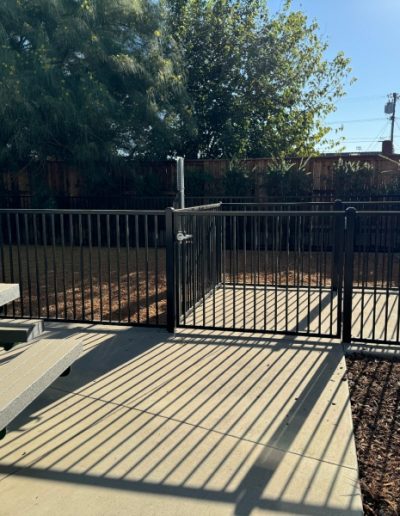 Black metal fence enclosing a small outdoor area with wood chips and a gate