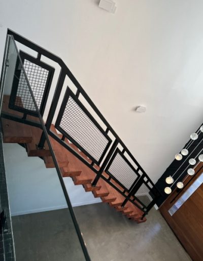 Modern staircase with a black metal railing and mesh panels, featuring wooden steps and a contemporary interior design