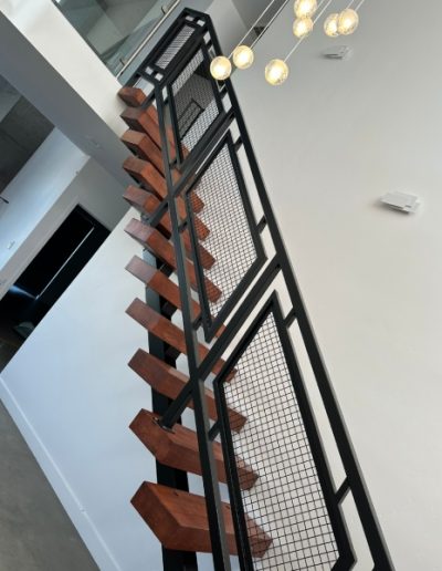 Sleek staircase with a minimalist design, showcasing a black metal railing and mesh panels against a white wall